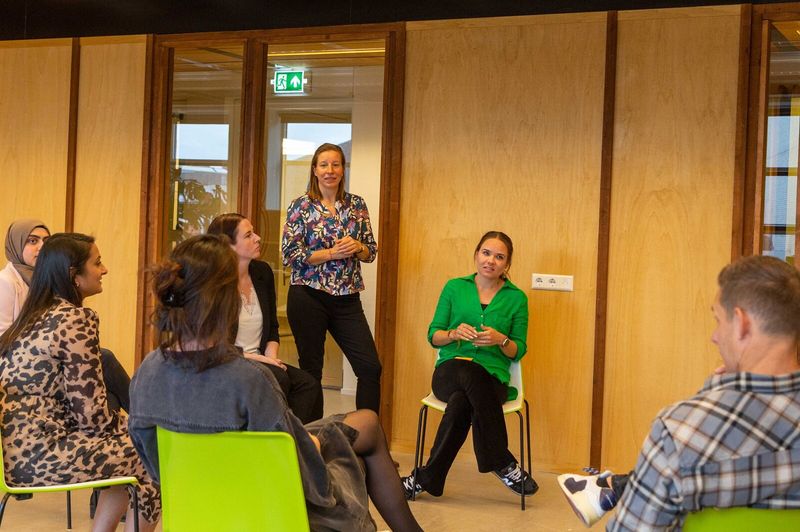 2 personen aan vergadertafel overleggen met 3 personen op een groot scherm